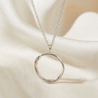 Silver circular pendant necklace on a soft beige fabric background