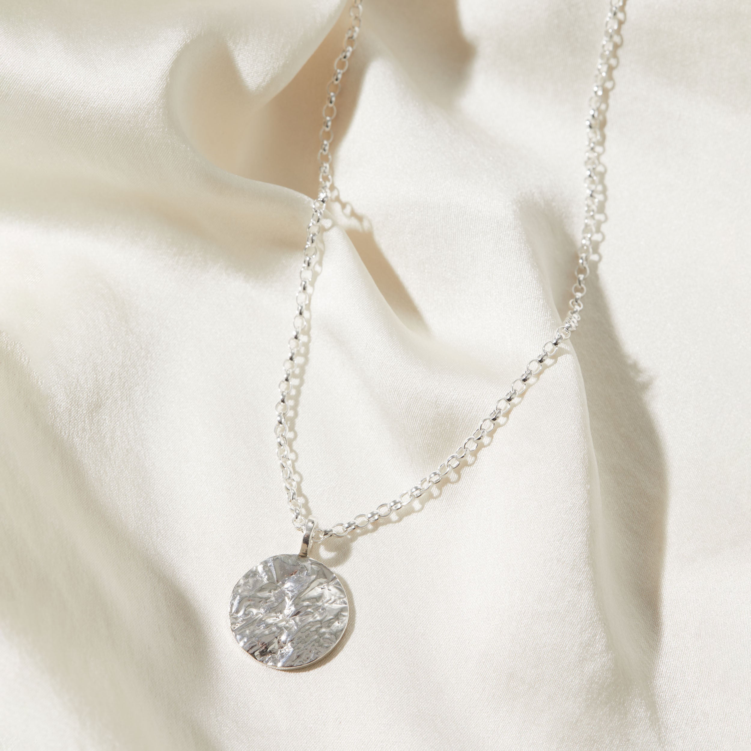 Silver necklace with a round bark textured pendant on a white fabric background
