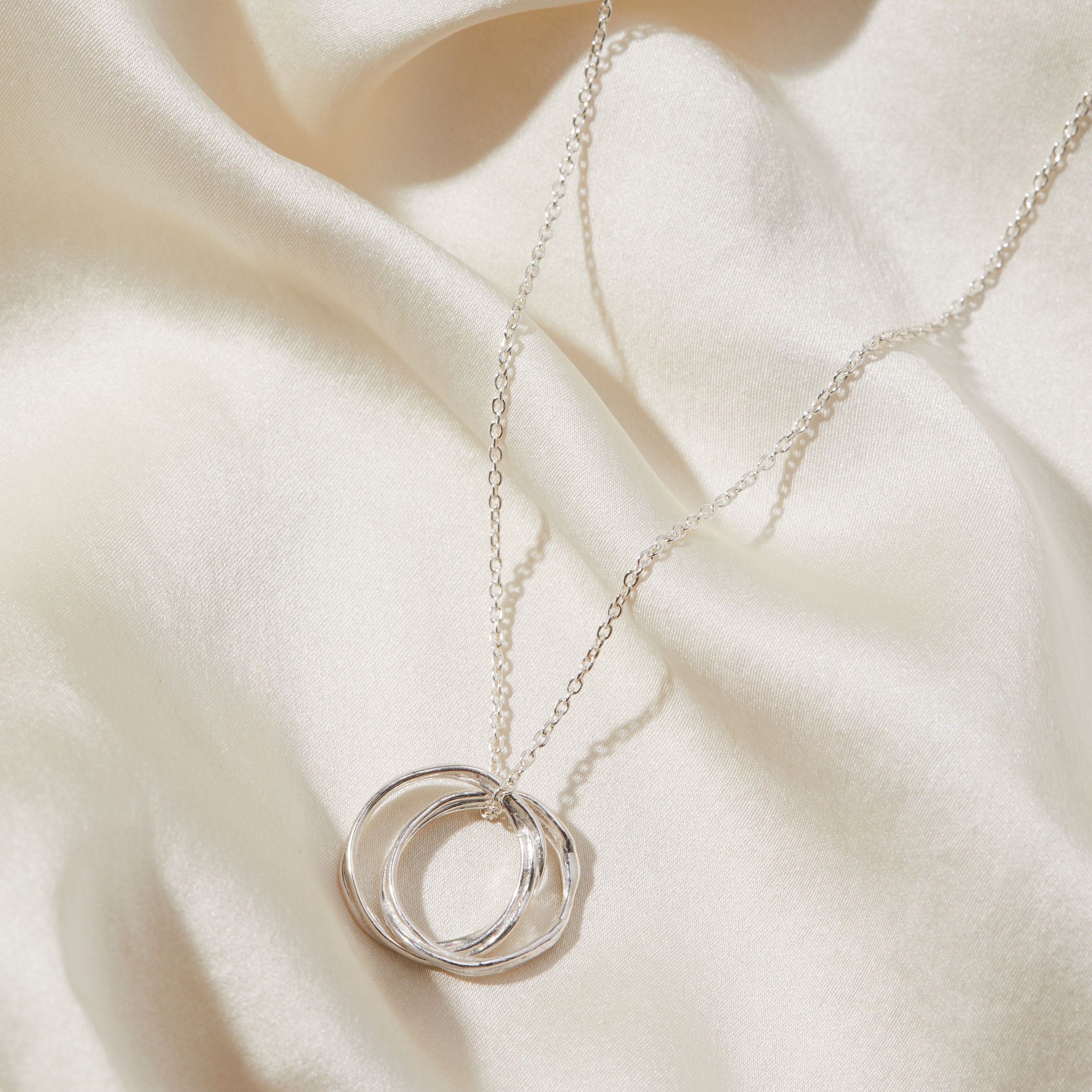 Silver necklace with a double-circle pendant on a beige fabric background