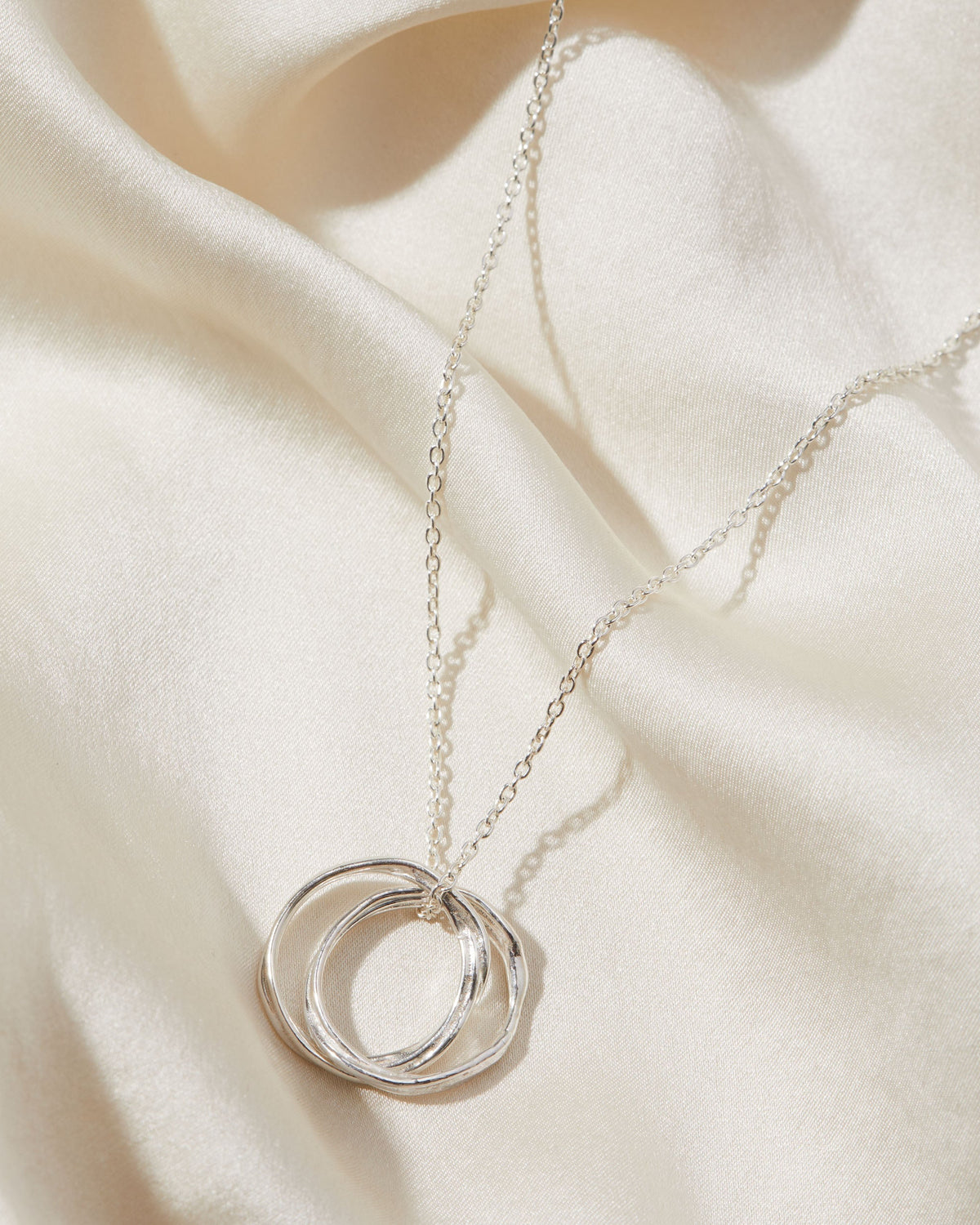 Silver necklace with a double-circle pendant on a beige fabric background