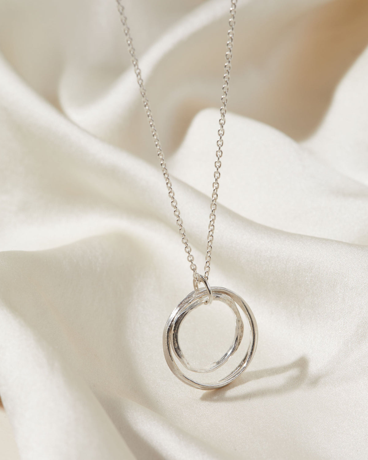 Silver necklace with a double-circle pendant on a white fabric background