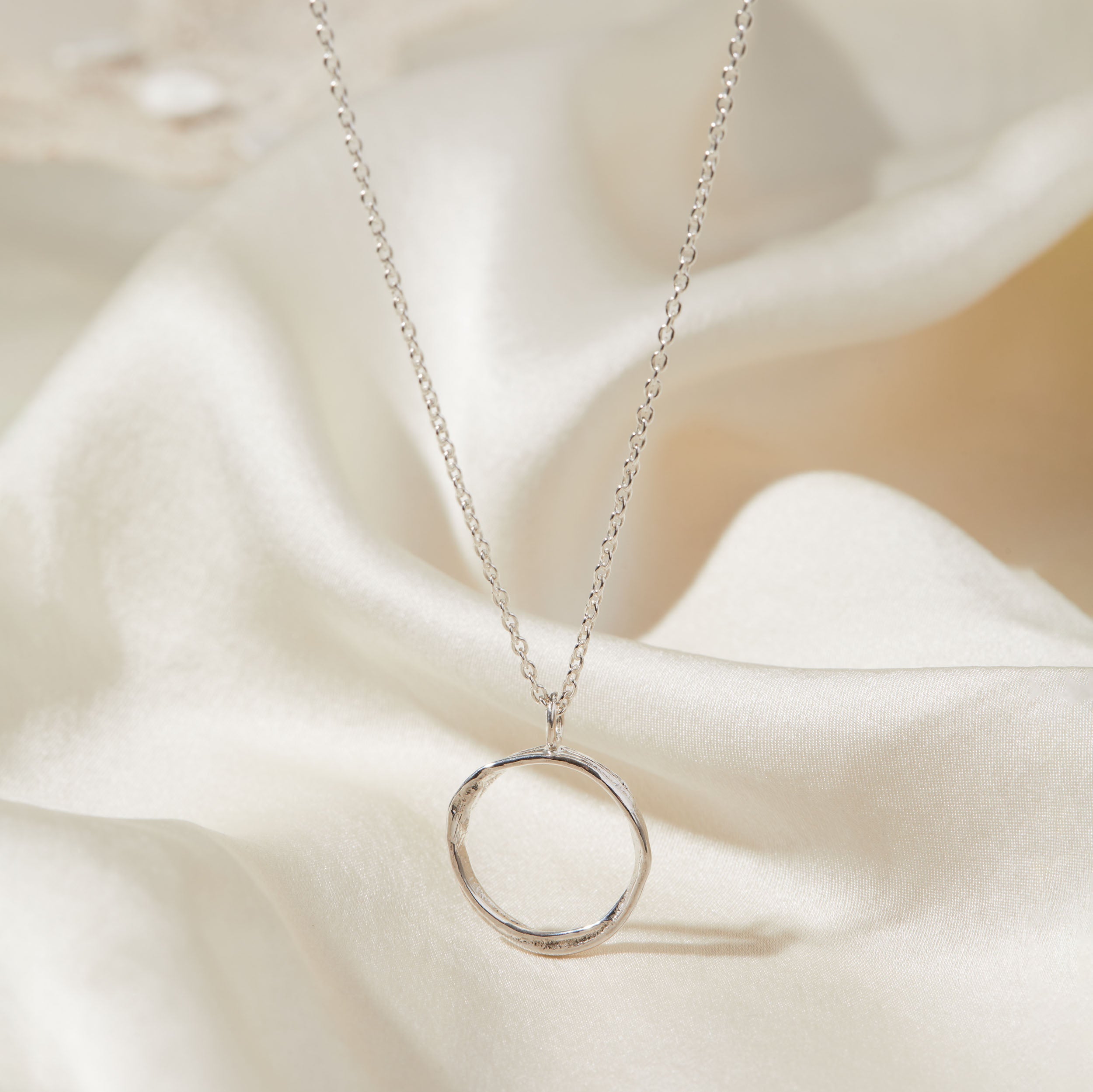 Silver necklace with a circular pendant on a soft fabric background