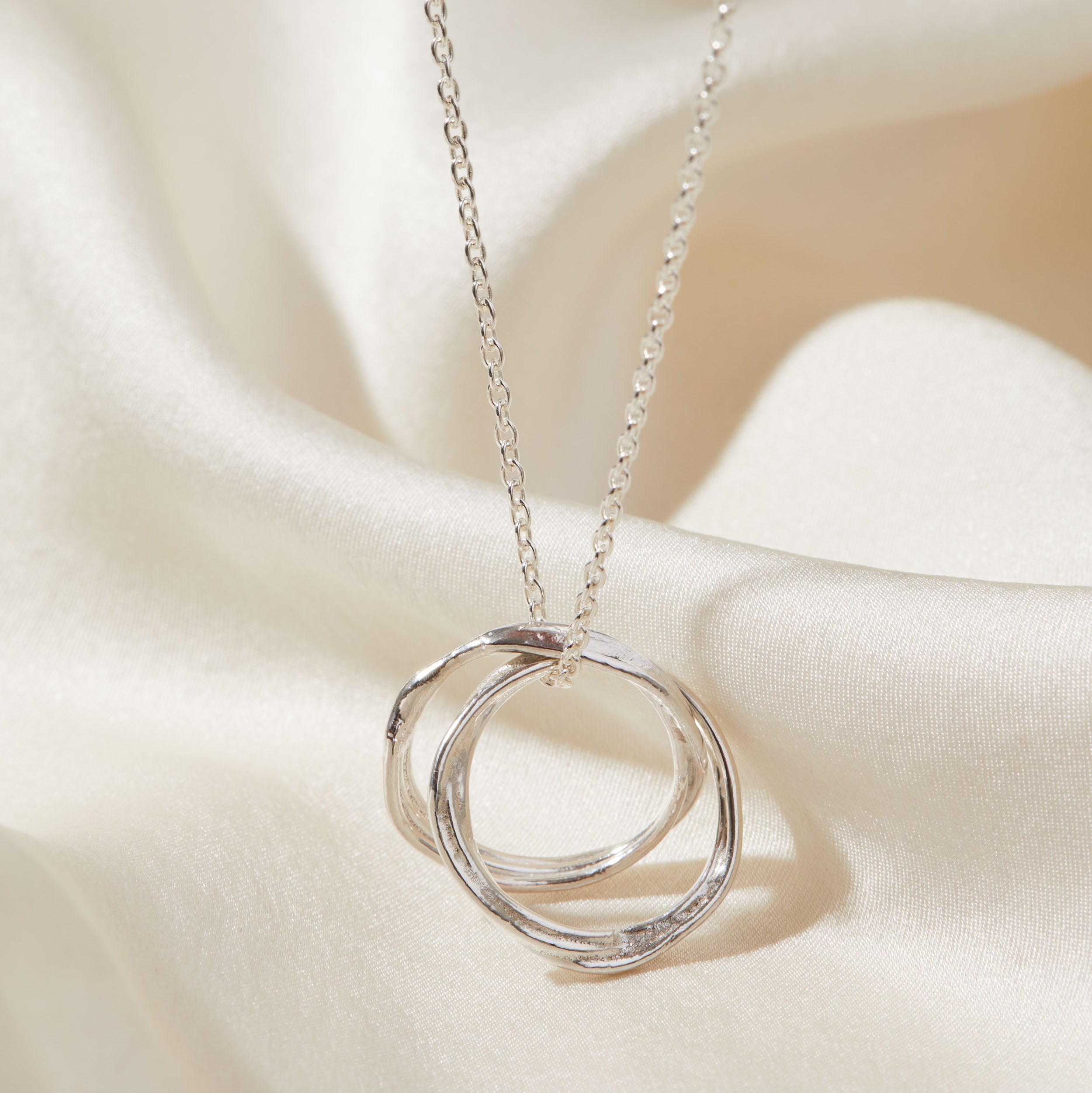 Silver necklace with a double ring pendant on a white fabric background