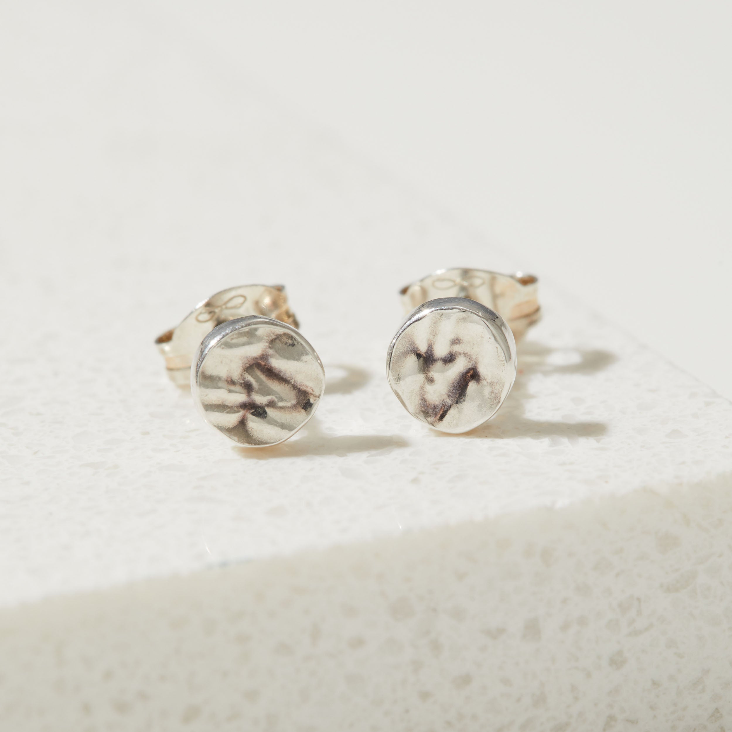 Pair of round earrings with tree textured design on a light background