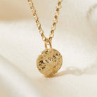 Gold necklace with a bark textured pendant on a beige background