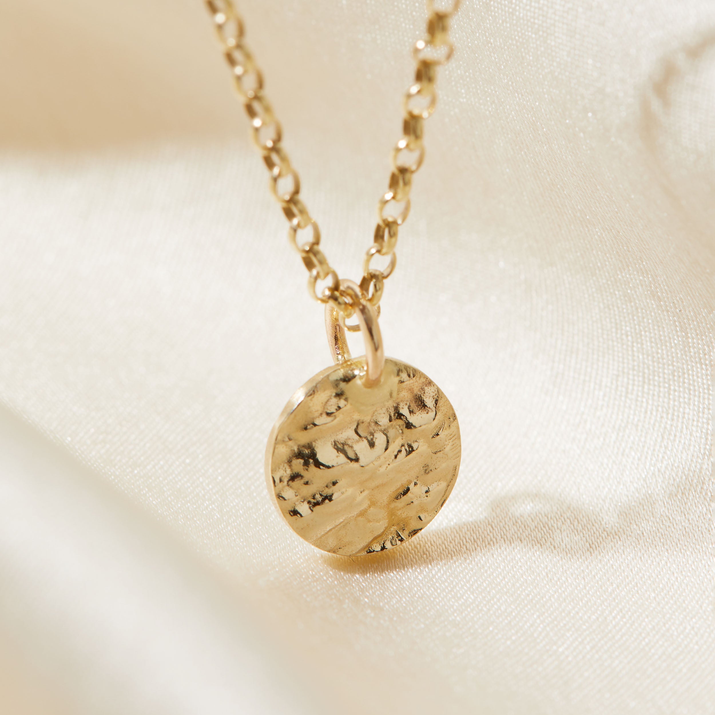 Gold necklace with a bark textured pendant on a beige background