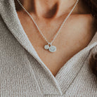 Necklace with heart and initial pendants worn by a person in a beige sweater.