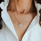 Necklace with a round phoenix pendant worn by a person in a white shirt.