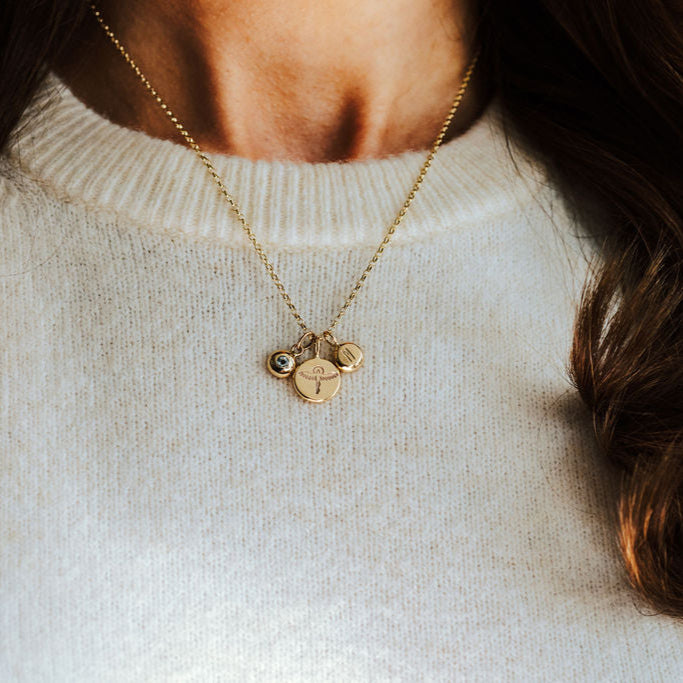 Woman wearing gold necklace with phoenix, initial and birthstone pendants.