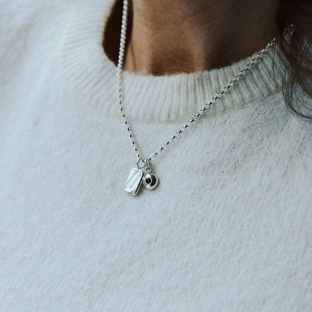 Woman in a white knitted t-shirt wearing a silver feather necklace with a birthstone charm.