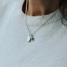 Woman in a white knitted t-shirt wearing a silver feather necklace with a birthstone charm.