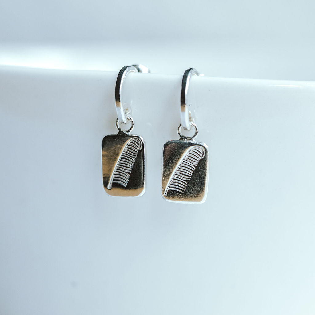 Sterling silver hoop earrings resting on a white bowl, featuring a charm with a feather design.