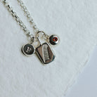 Charm necklace on a white background featuring a feather, an initial and a birthstone.