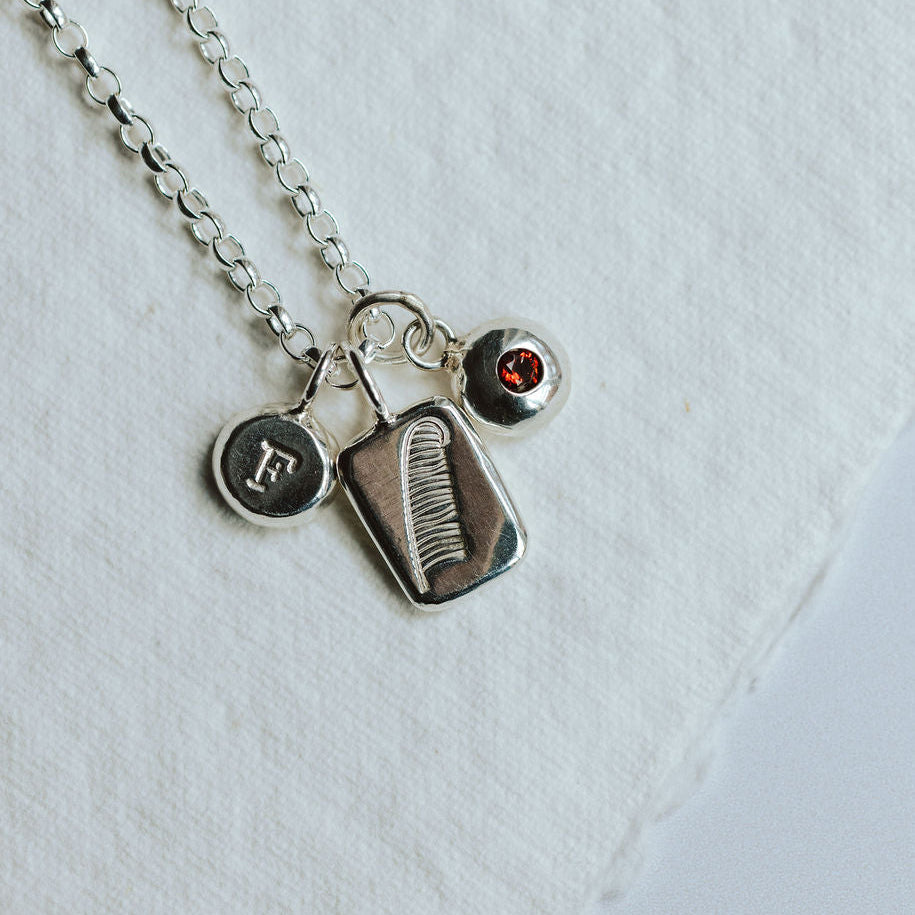 Charm necklace on a white background featuring a feather, an initial and a birthstone.