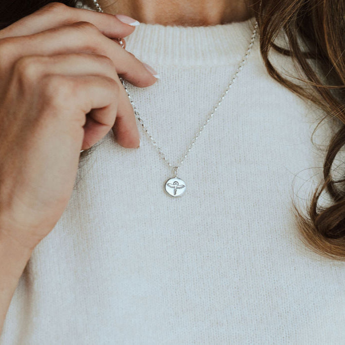 Person wearing a phoenix necklace on a white knitted t-shirt