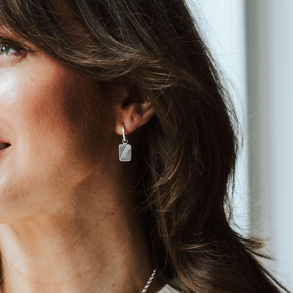 Woman with dark hair wearing a pair of hoop earrings with feather charms.