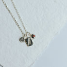 Necklace with three charms on a white background, featuring a feather design, and initial and a birthstone charm.