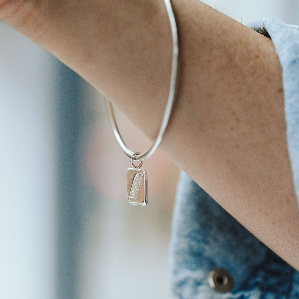 Woman wearing a denim shirt with a silver bangle on her wrist featuring a feather charm.