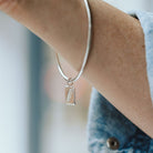 Woman wearing a denim shirt with a silver bangle on her wrist featuring a feather charm.