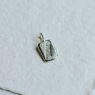Square shaped silver charm with a stamped feather detail on a white paper background.