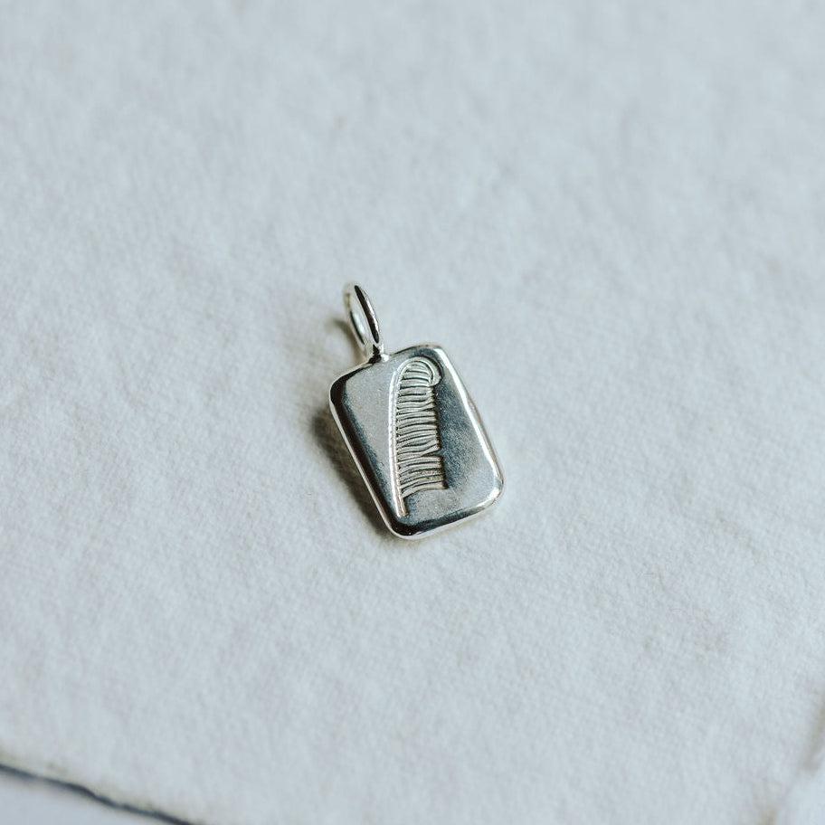 Square shaped silver charm with a stamped feather detail on a white paper background.
