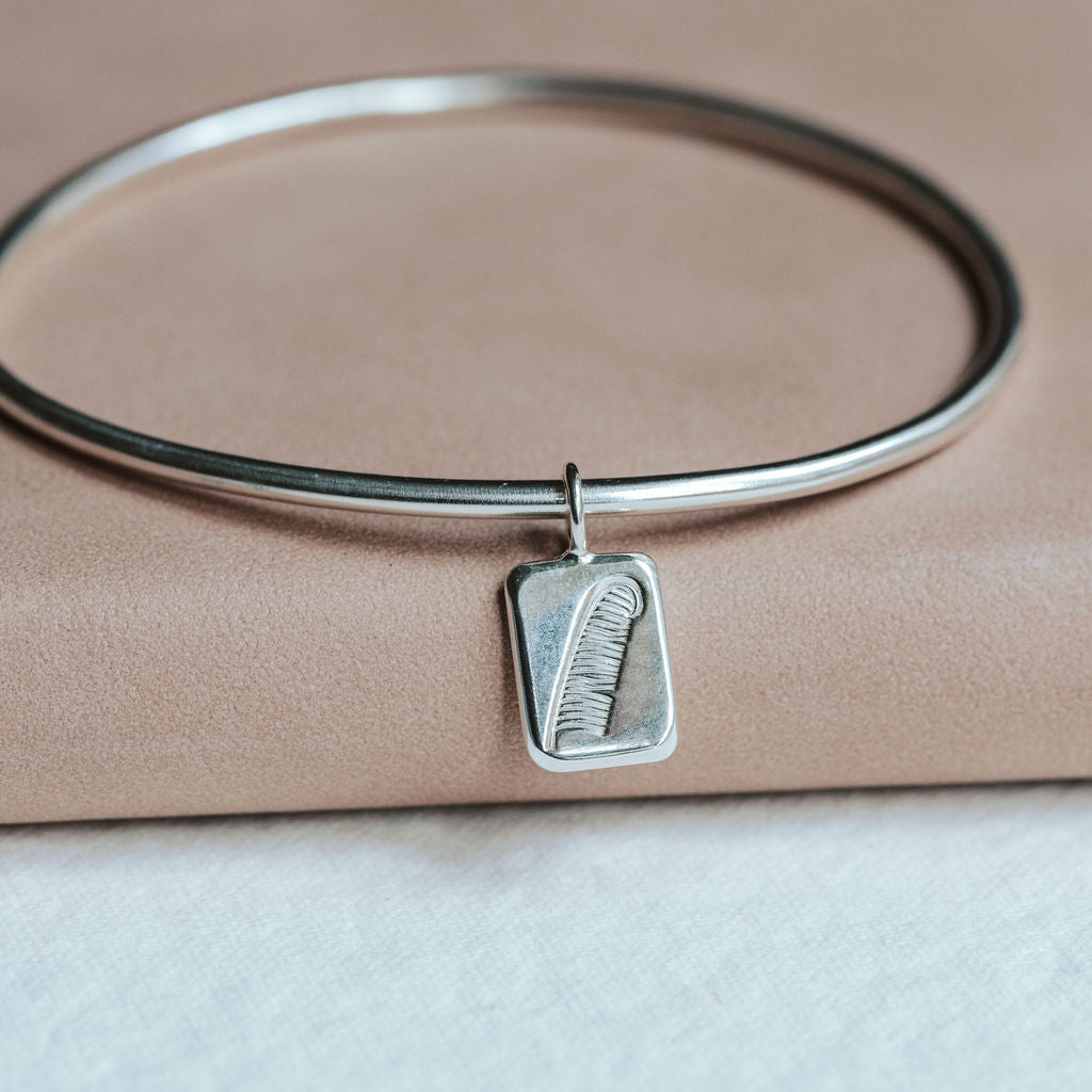 Silver bangle with a feather charm on a pink book.