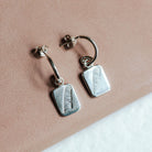 Sterling silver hoop earrings with feather charms resting on a pink book.
