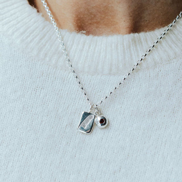 Woman in a white knitted t-shirt wearing a charm necklace with a feather design on it and a birthstone.