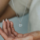Silver phoenix pebble necklace held in a hand against a neutral background