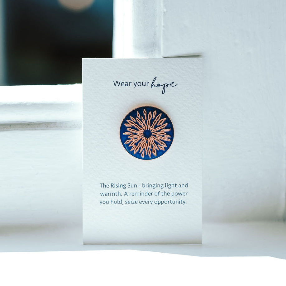Sunrise design on a blue pin badge on a white card.