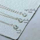 Three silver necklaces with different chain styles on a textured surface.