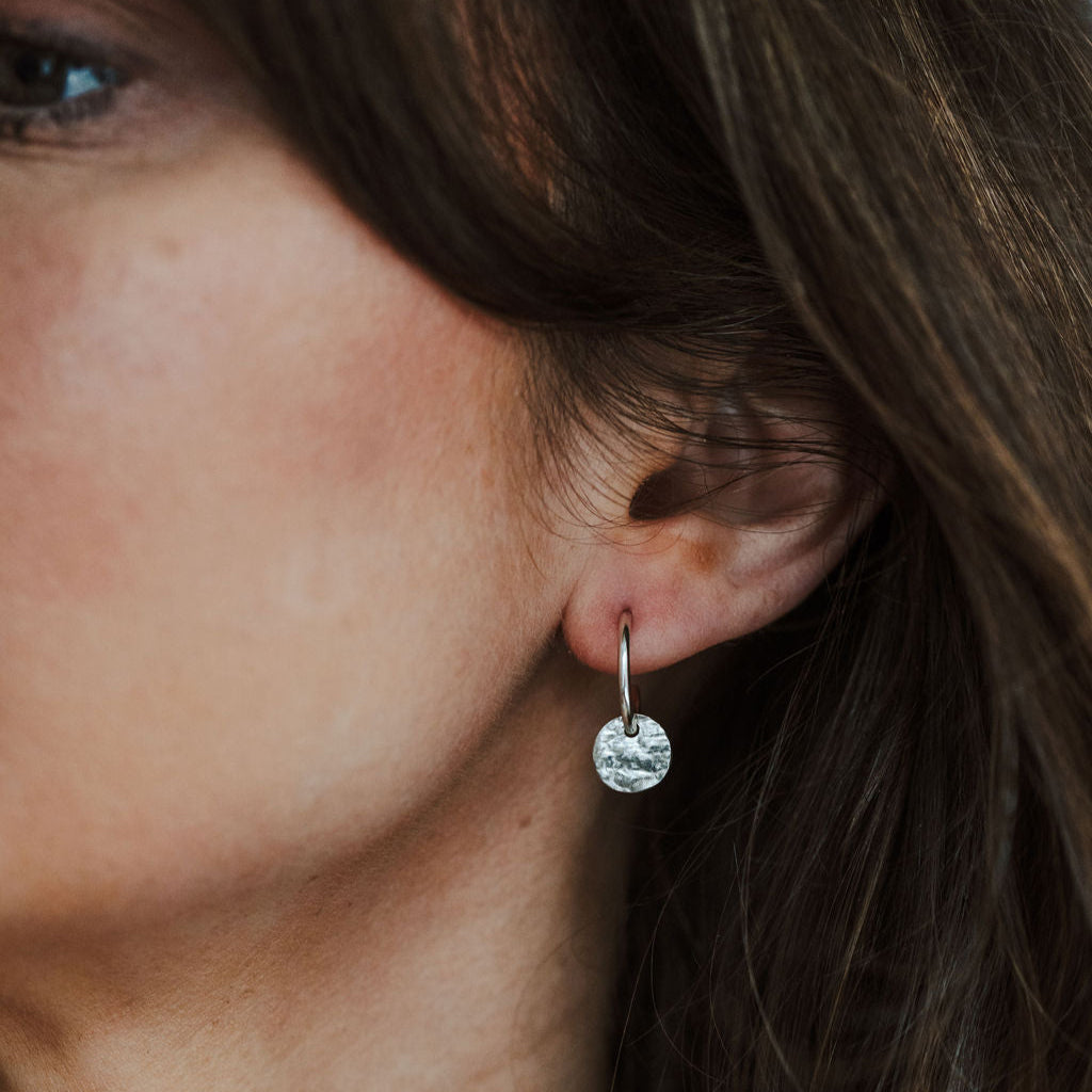 Close-up of a person wearing a silver earring with a tree bark textured charm.