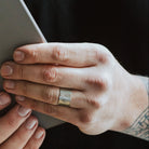 Man wearing a ring with sunrise design holding a grey notebook.
