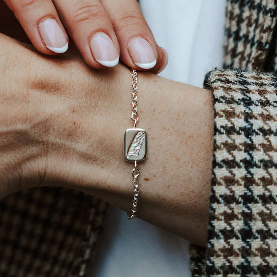 lady wearing a silver bracelet with a square charm and a feather motif