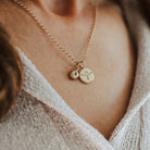 Close-up of a person wearing a gold necklace with birthstone and phoenix pendants.