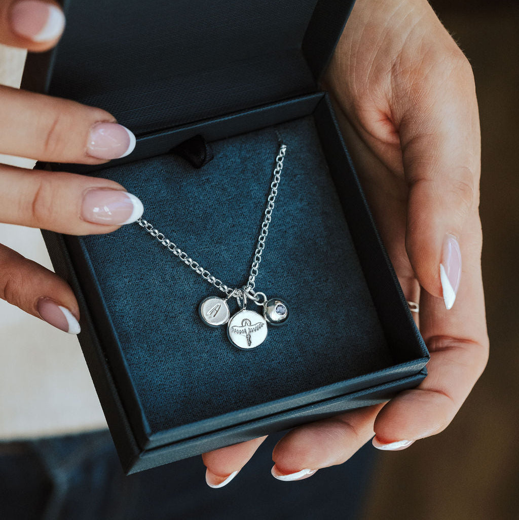 Silver necklace with charms held in a blue jewellery box by hands with light nail polish.