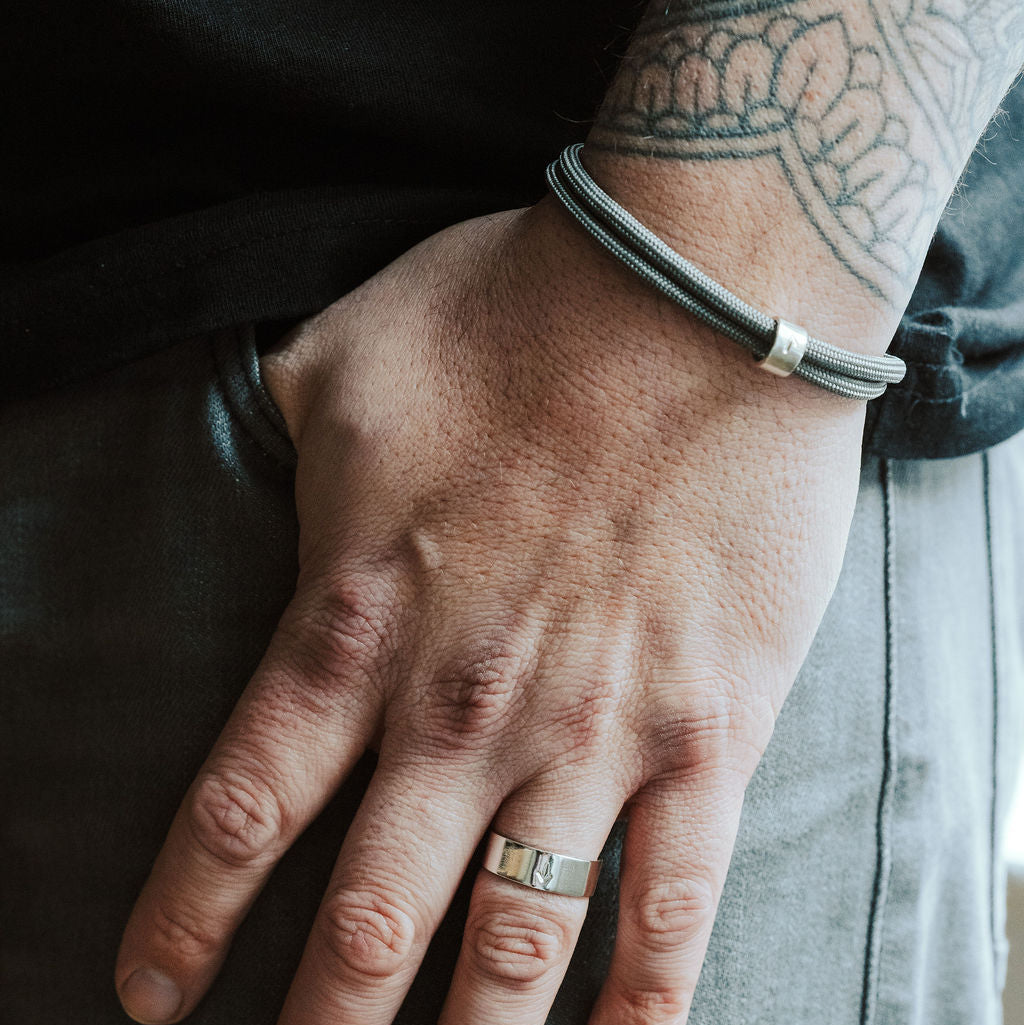 Hand with a ring and bracelet, wearing a black leather jacket and gray pants.
