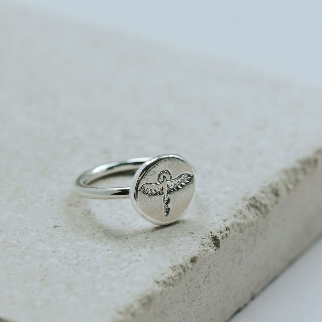 Silver ring with a phoenix design on a textured stone surface