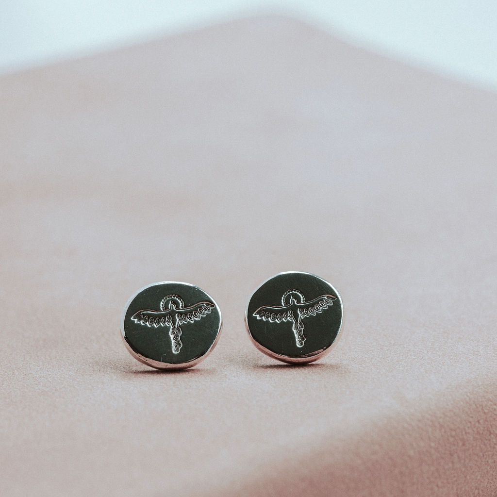 Silver round earrings with silver designs on a pink surface