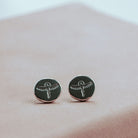 Silver round earrings with silver designs on a pink surface
