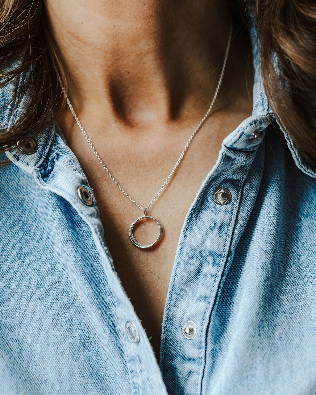 Woman in a denim shirt wearing a silver circle necklace.