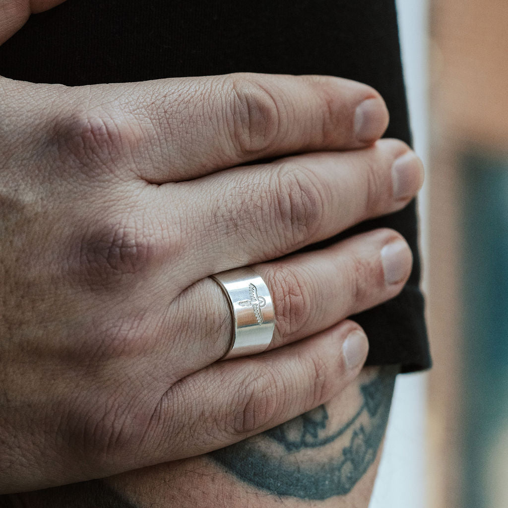 Hand wearing a silver ring with tattoos on the arm, blurred background