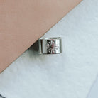 Silver ring with a heart design on a light pink and white background