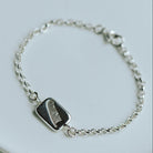 silver bracelet with a charm with a feather motif on a white dish