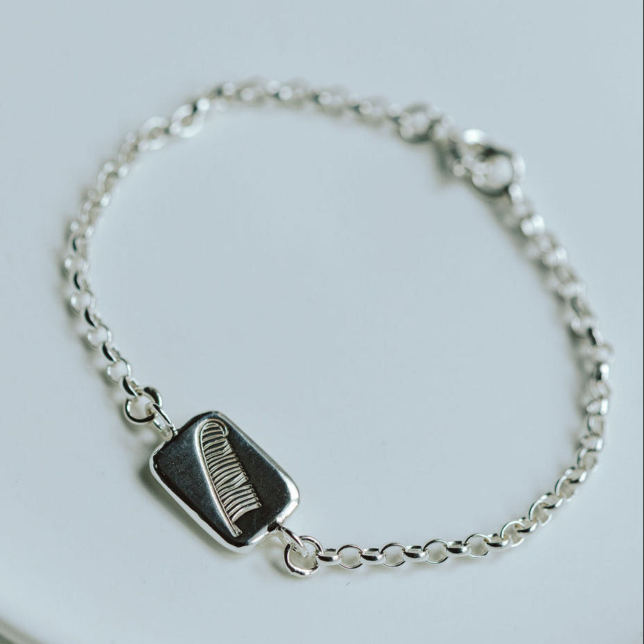 silver bracelet with a charm with a feather motif on a white dish