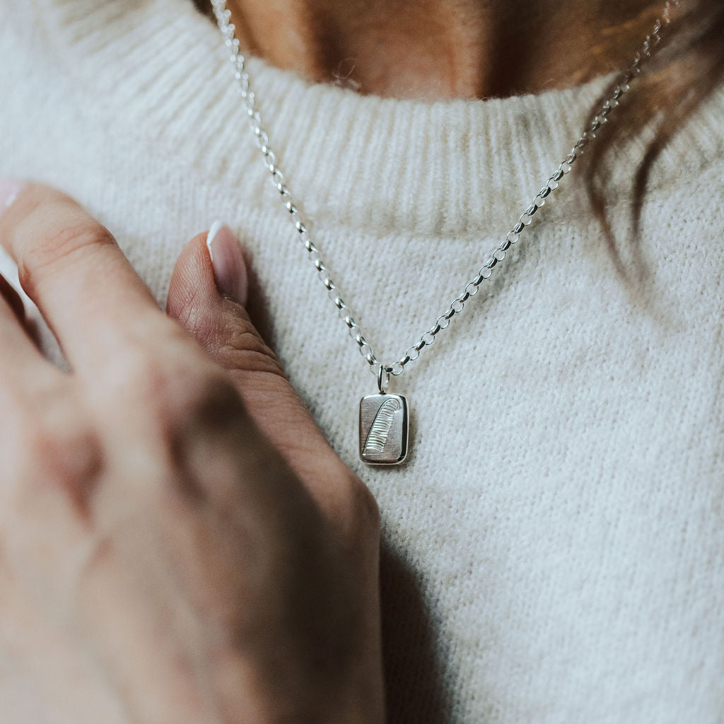 woman wearing a white knitted t-shirt and a necklace with a pendant featuring a feather design.