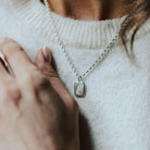 woman wearing a white knitted t-shirt and a necklace with a pendant featuring a feather design.