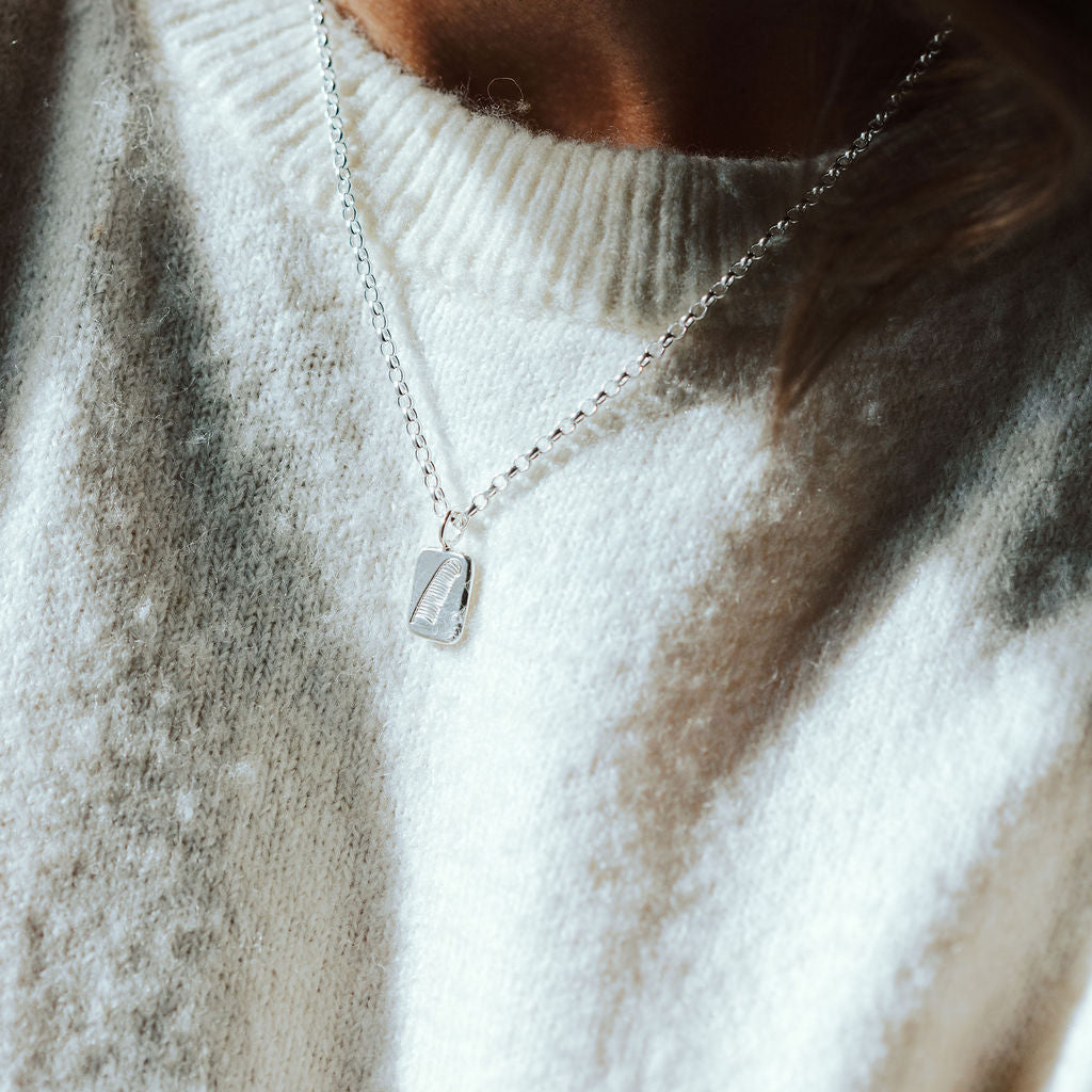 woman in a pale knitted tee wearing a silver necklace with a feather motif