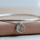 Silver bangle with a circular sunrise pendant on a beige surface
