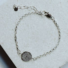 Silver bracelet with a circular sunrise charm on a light gray surface